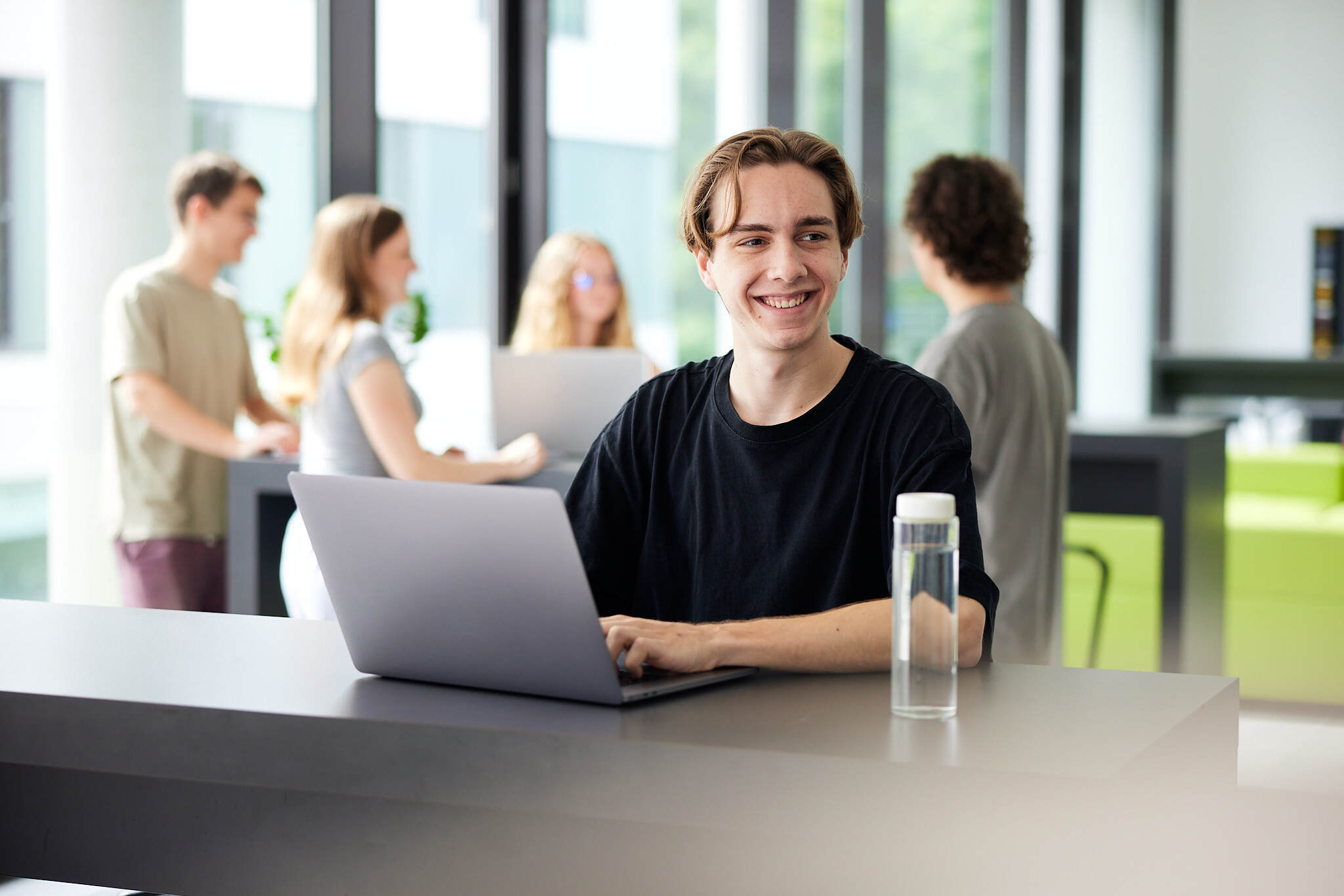 Ein junger Student sitzt hinter seinem Laptop in einem Aufenthaltsraum der FH Hagenberg und blickt seitlich über seine Schulter
