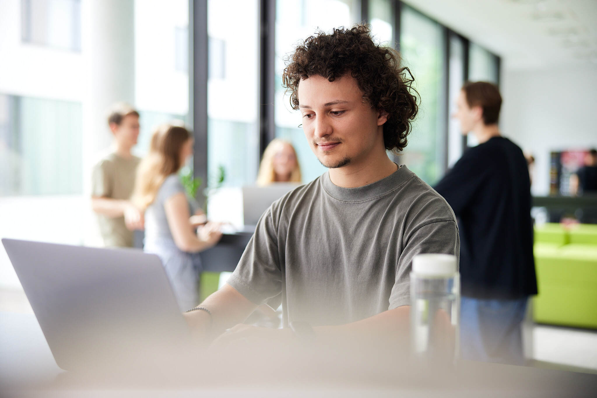 Ein junger Student sitzt hinter seinem Laptop in einem Aufenthaltsraum der FH Hagenberg und wird dabei von der Seite abgebildet