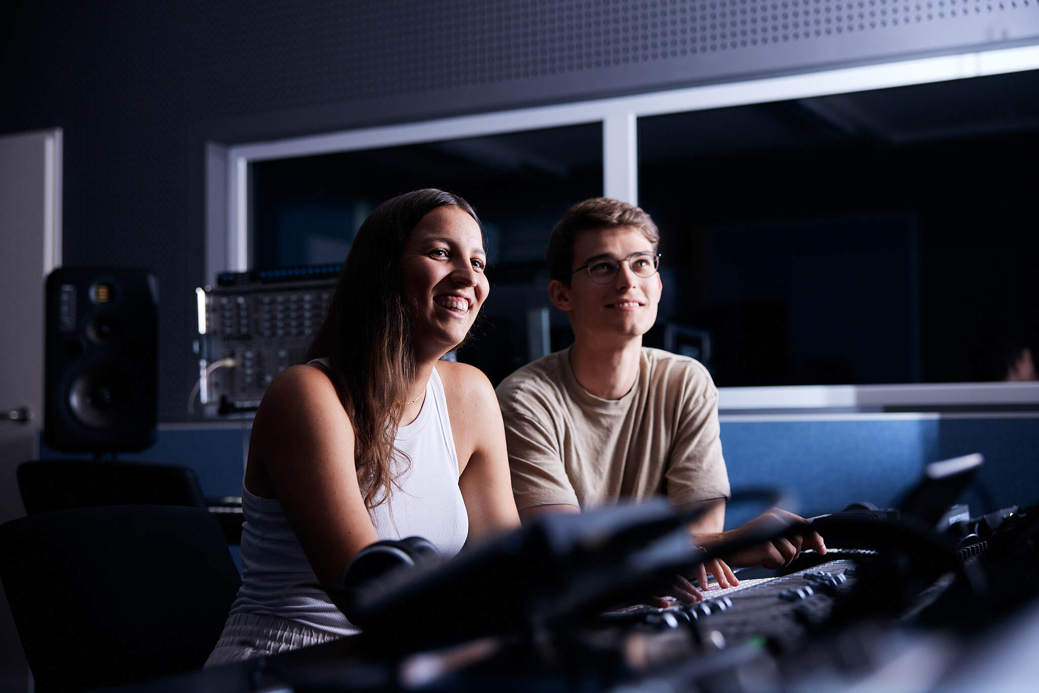 zwei junge Studenten sitzen in einem dunklen Raum und schauen gemeinsam auf einen Bildschirm der ihre Gesichter beleuchtet.