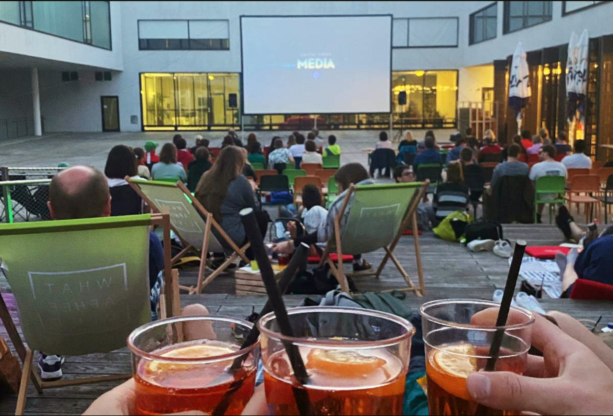Personen auf Liegestühlen und Sesseln im Innenhof des FH-Gebäudes, die gemeinsam eine Film auf der großen Leinwand im Rahmen des FH Open Air Sommerkinos genießen