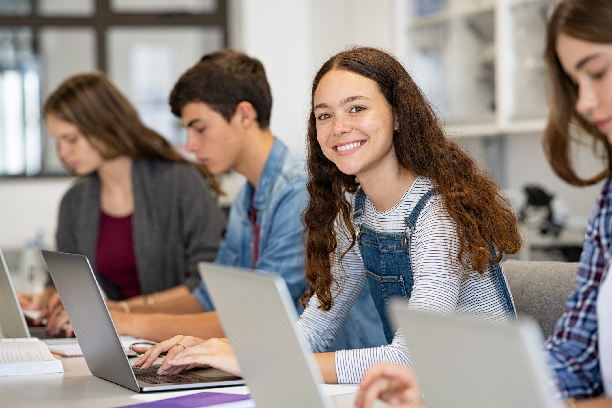 Vier Schüler*innen sitzen vor Laptos, ein Mädchen lächelt in die Kamera.