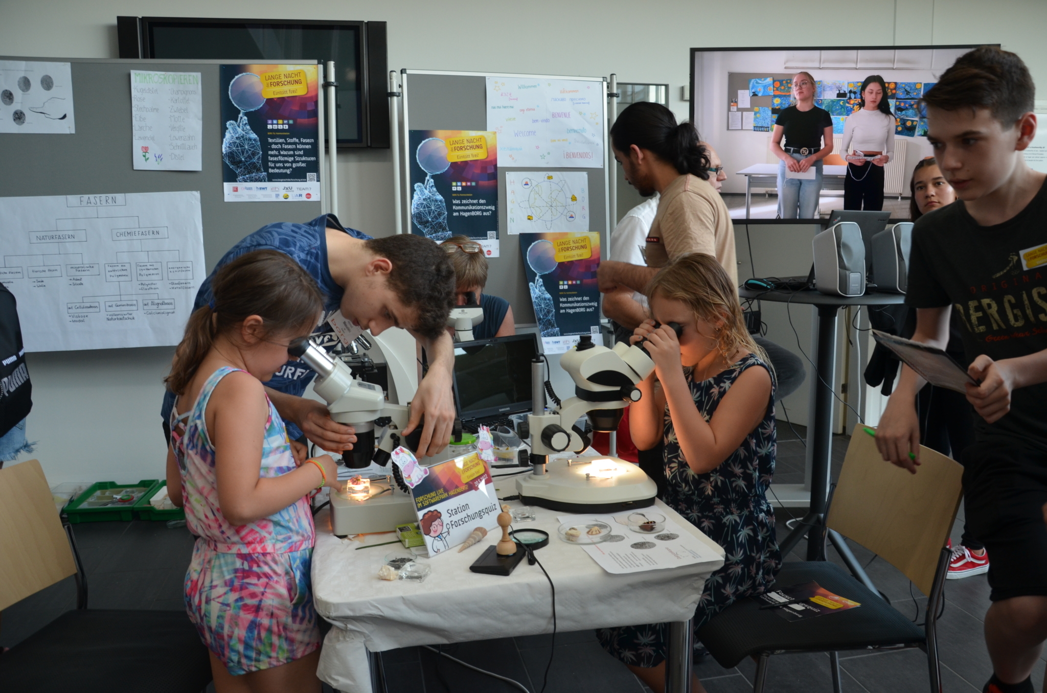 Kinder dürfen duch ein Mikroskop etwas ansehen und eine Student erklärt