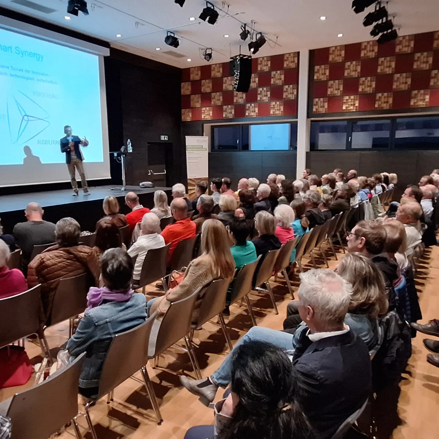 Ein Hörsaal gefüllt mit Personen hochen sich einen Vortrag von Professor Stephan Winkler an