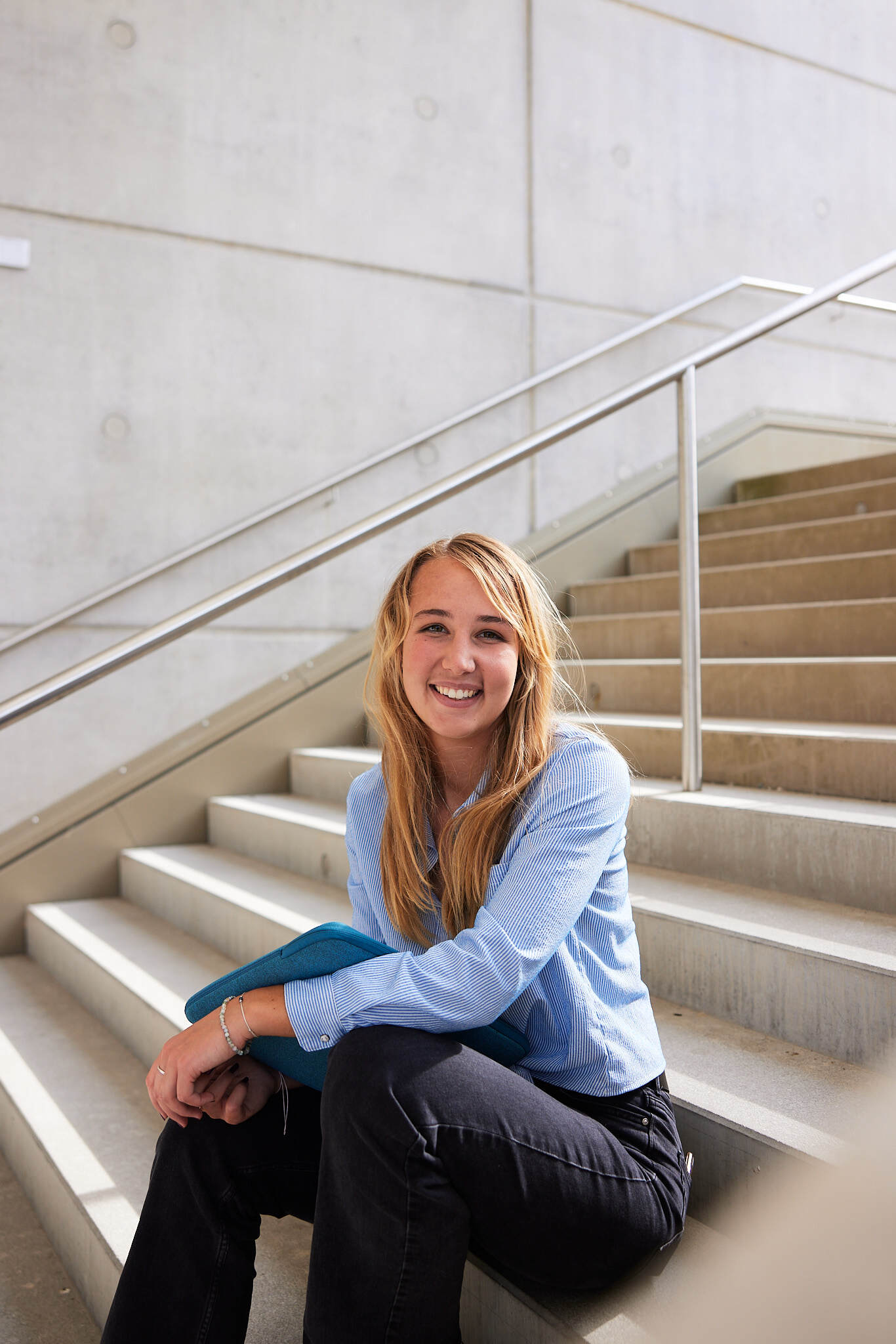 eine junge Studentin sitzt auf einer Treppe am Campus der FH Steyr und wird von der Seite abgebildet.