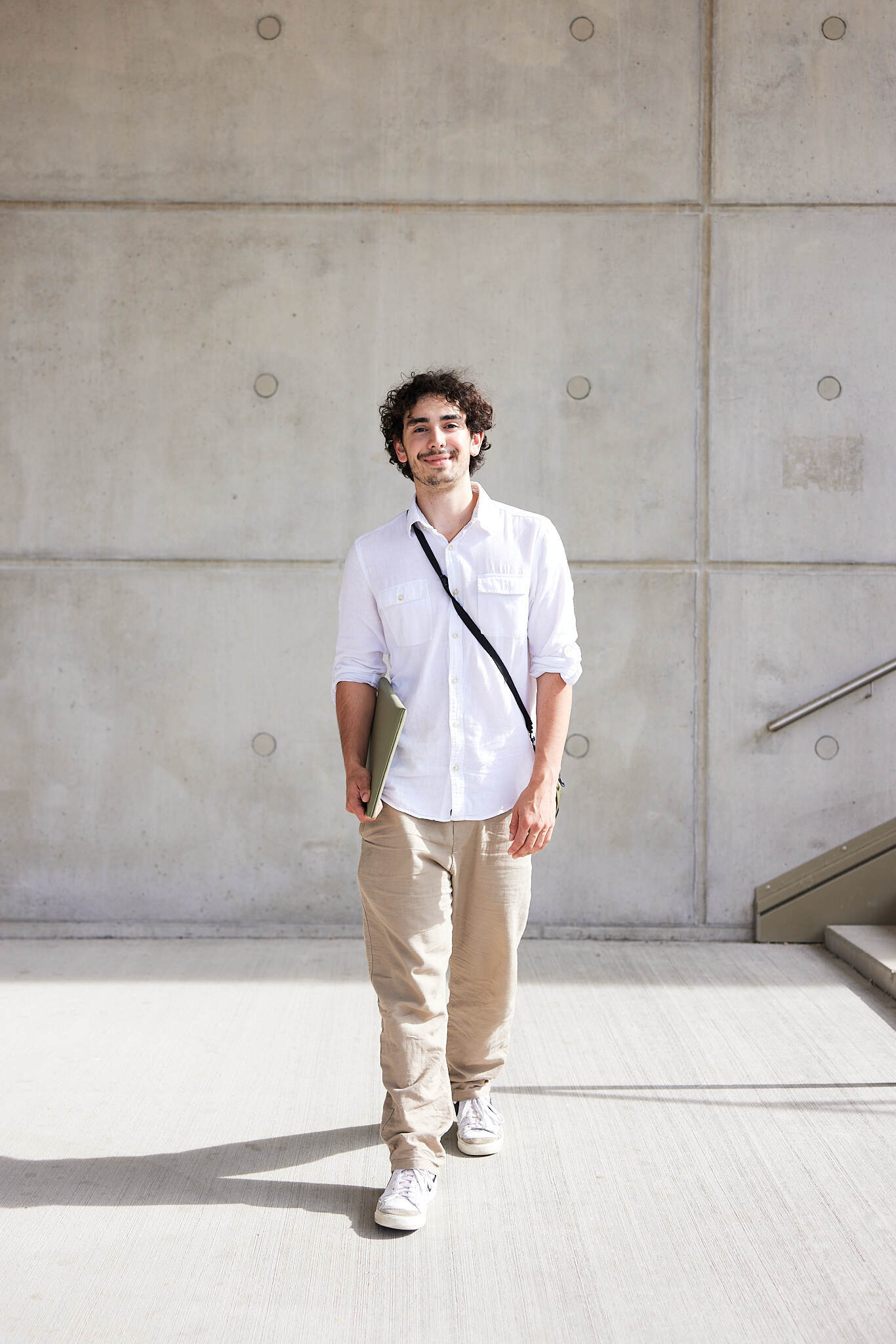 ein junger Student wird komplett von vorne vor einer Treppe am Campus Steyr abgebildet.