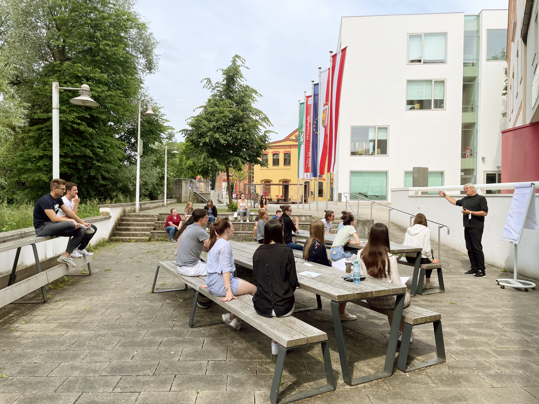 Mehrere Studierende sitzen im Freien vor der FH OÖ Campus Steyr und nehmen gemeinsam an einer Lehrveranstaltung teil