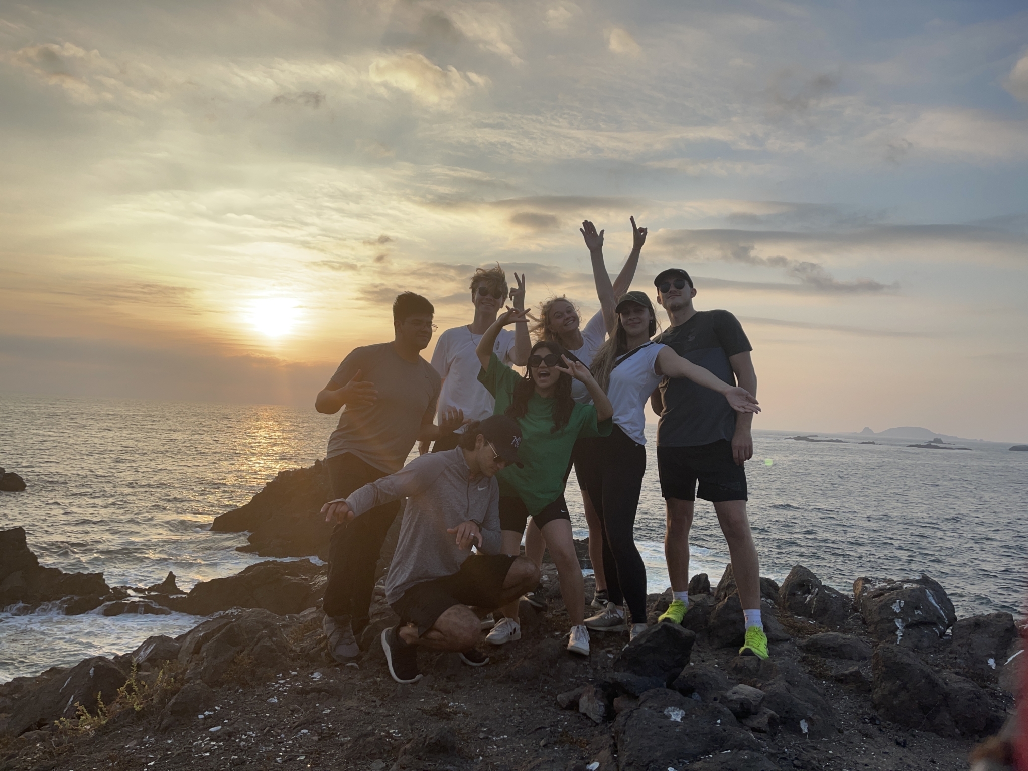 Eine Gruppe junger Menschen steht am Meer bei Sonnenuntergang