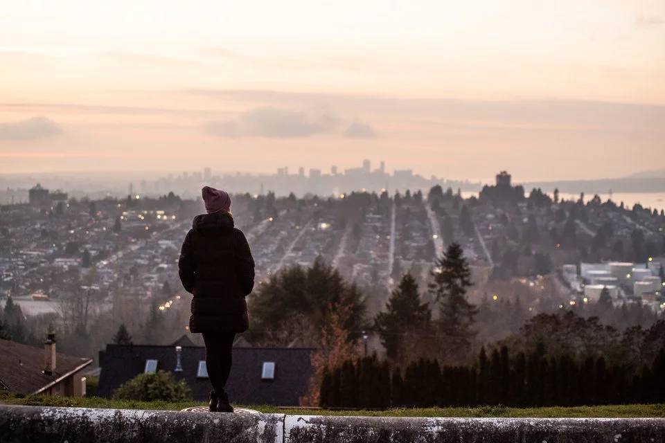 Eine Frau von hinten, die auf eine Stadtlandschaft bei Sonnenuntergang blickt