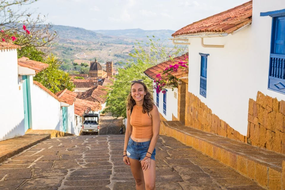 Eine junge Dame steht in einer schmalen Gasse und blickt lächelnd in die Kamera