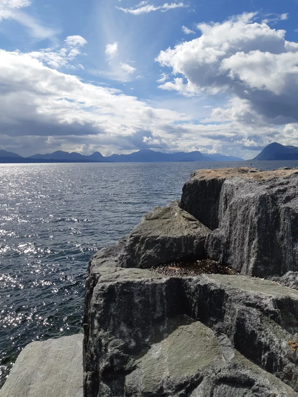 Naturaufnahme einer Steinküste mit Meerblick und Hügel in der Ferne