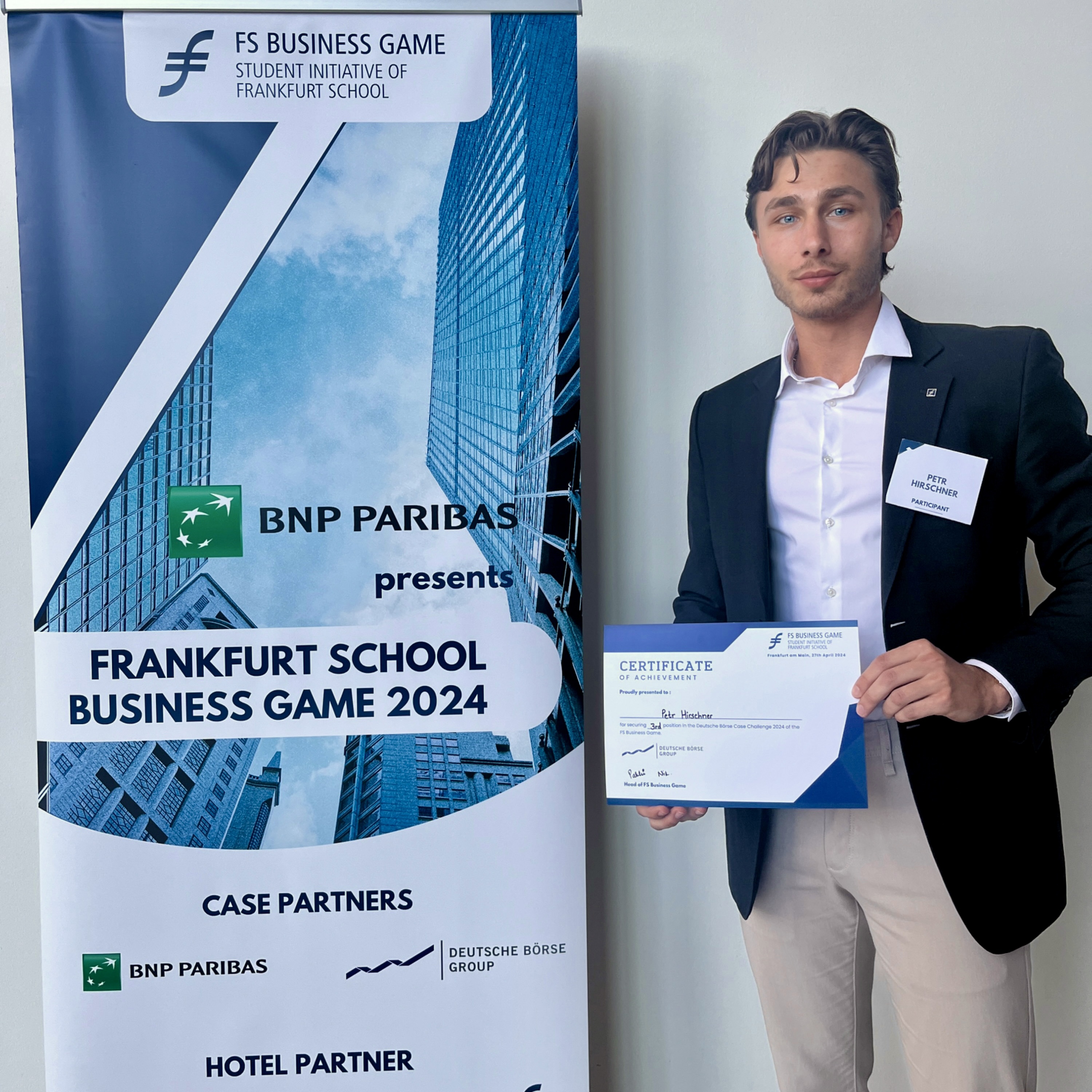 Peter Hirschner hält ein Zertifikat in der Hand und steht neben einem Aufsteller des Frankfurt School Business Game 2024