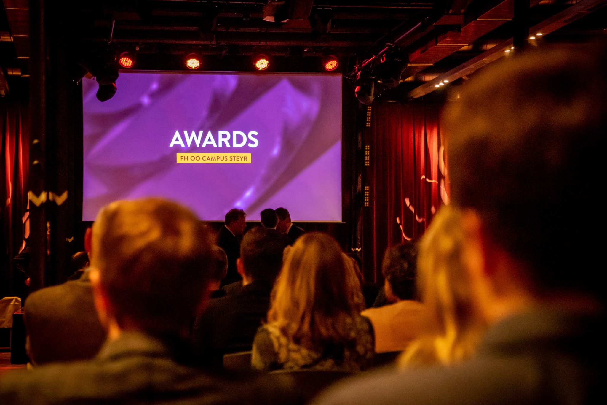 Foto aus der Publikumsperspektive in Richtung Bühne, auf der gerade die Präsentationsfolie ‚Awards‘ zu sehen ist