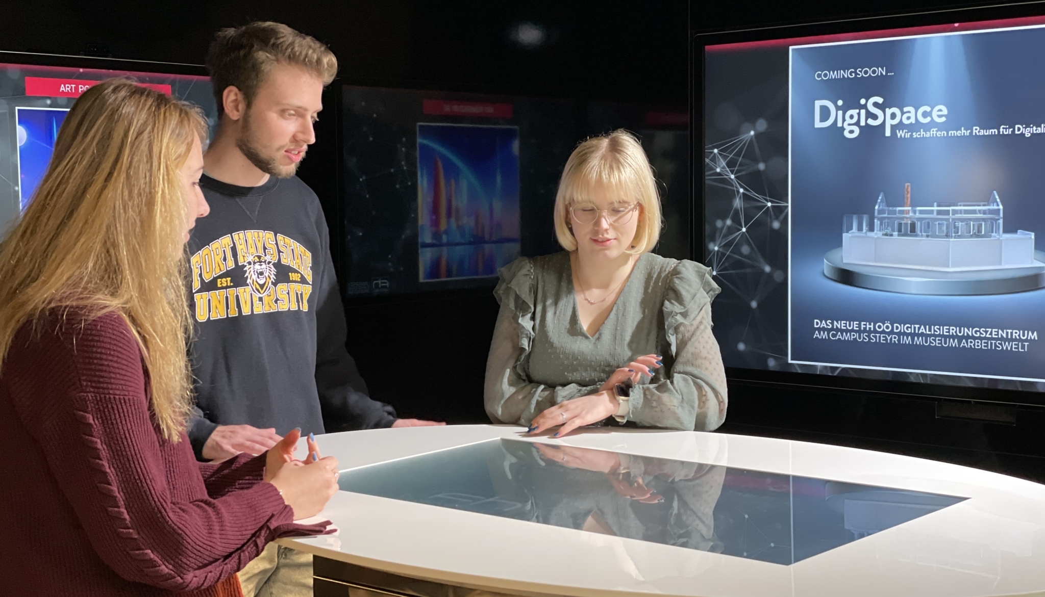 Eine Gruppe von Studierenden steht um einen Tisch im DigiSpace und bedient gemeinsam einen interaktiven Touchscreen