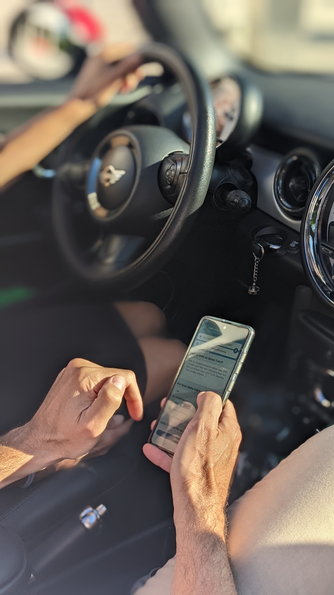 Foto einer Hand, die im Auto ein Smartphone mit einer geöffneten App hält.