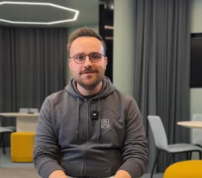 Im Fokus ist ein Mann, der auf einem Stuhl sitzt und in Richtung Kamera blickt