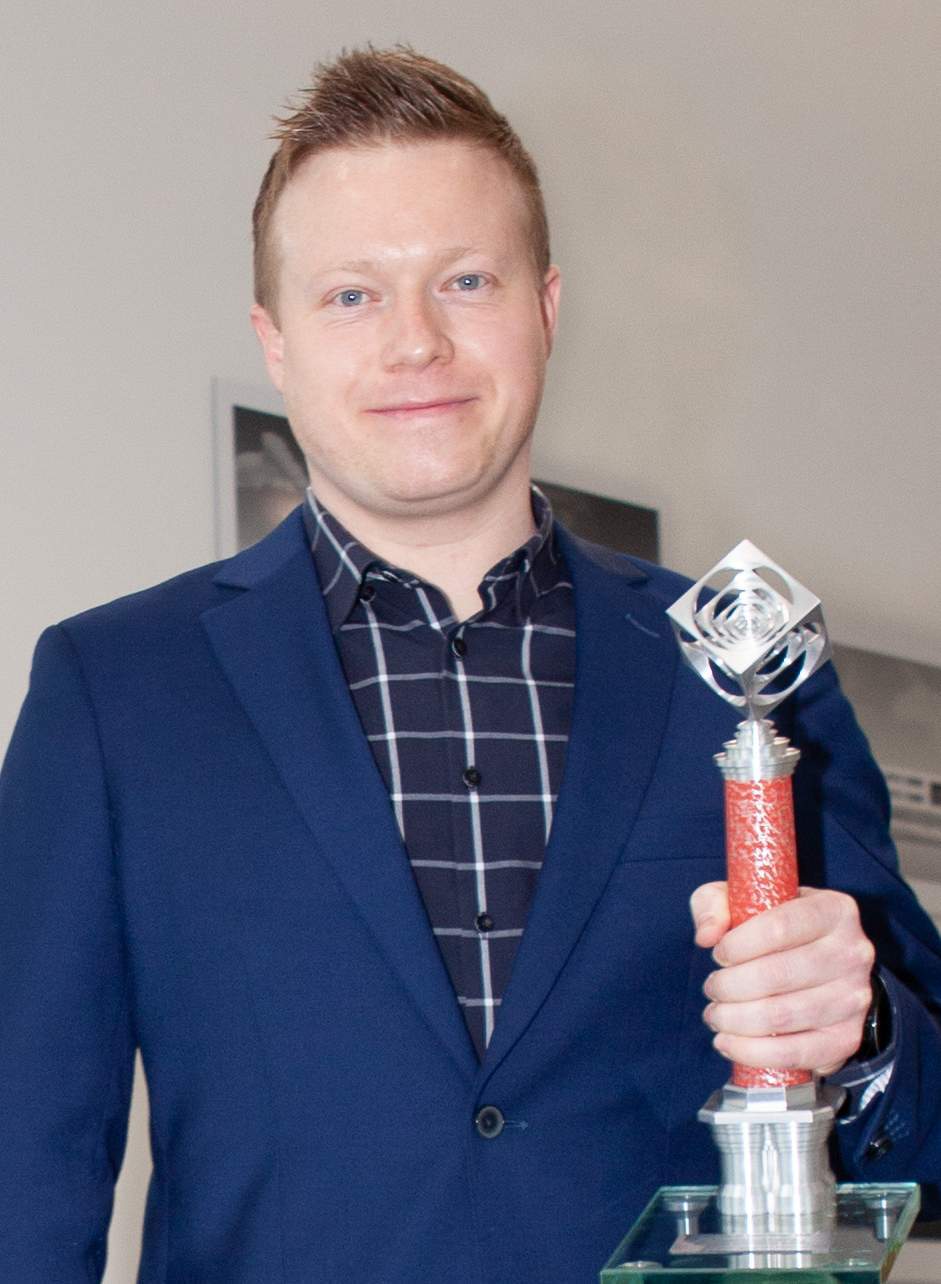 Auf dem Foto hält der Absolvent lächeln seinen Chimney Award in der Hand.