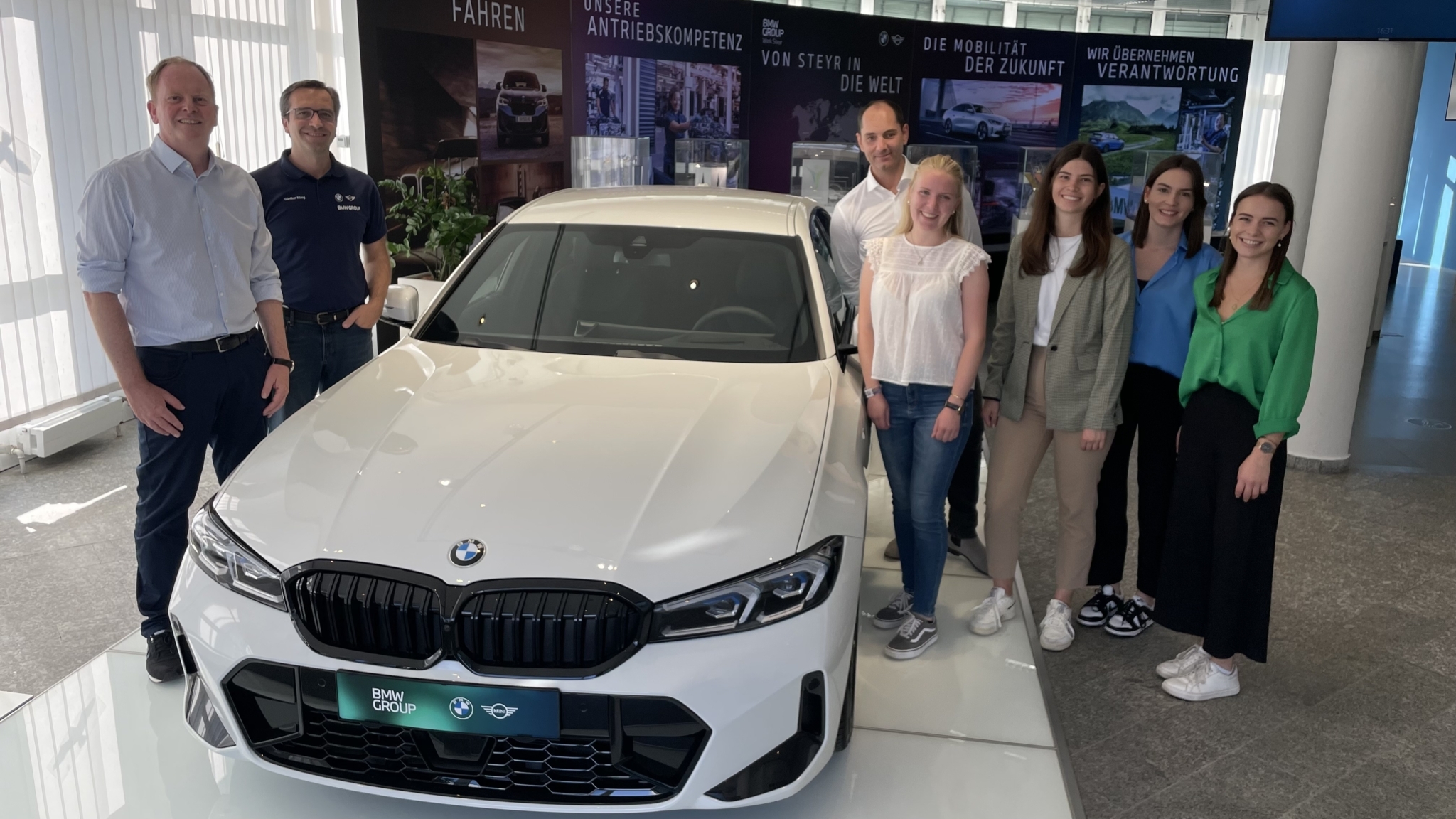 Auf dem Foto steht das Projektteam und ihre Betreuer bei einem BMW-Auto für ein Gruppenfoto zusammen.