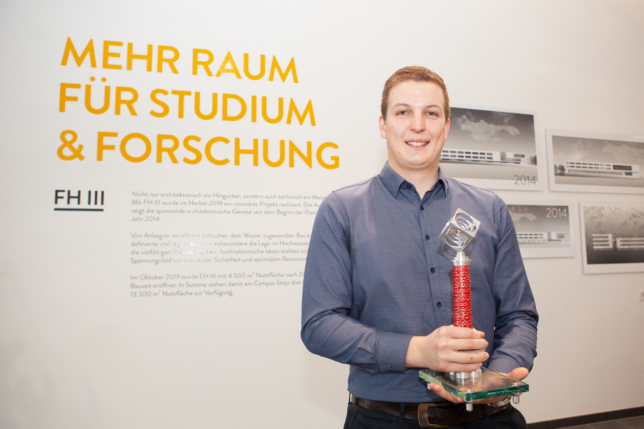 Auf dem Foto hält der Absolvent Alexander Strauß seinen Chimney Award in den Händen und lächelt.