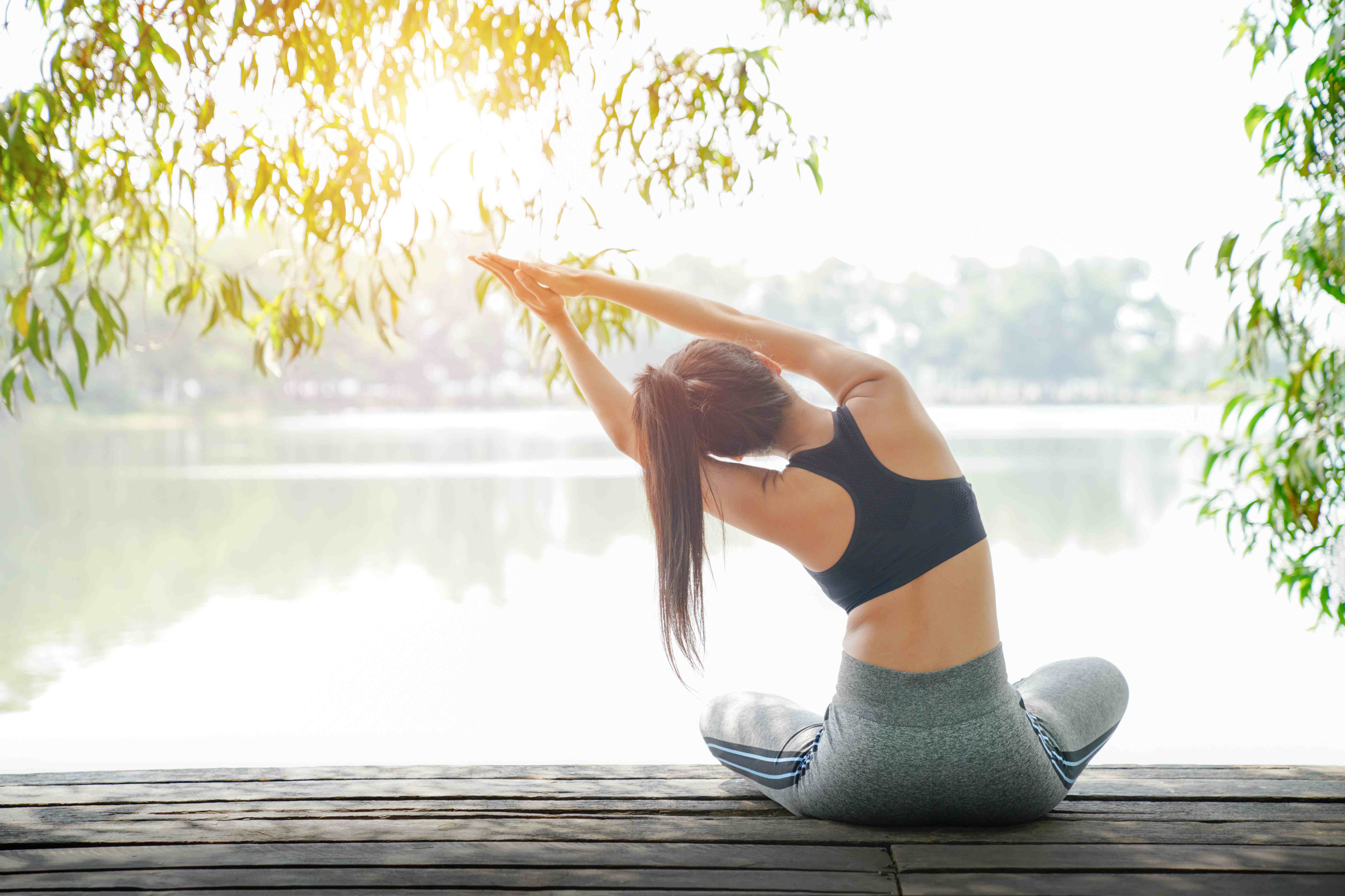 Eine Frau die Auf einem Steg vor einem See eine Yoga-Übung ausführt.