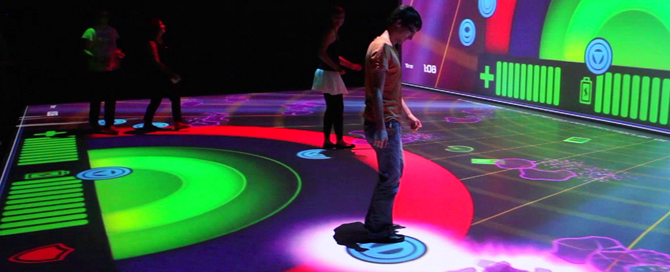 Mehrere Personen interagieren mit einem Videospiel, welches auf den Boden projiziert wird.