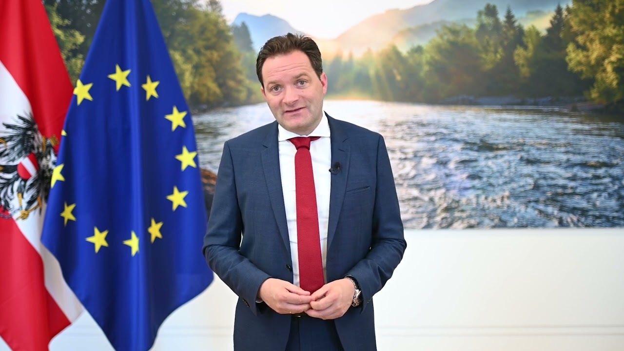Bundesminister Norbert Totschnig steht im Mittelpunkt des Bildes. Links neben ihm sind eine österreichische Flagge und daneben eine Europäische Union-Flagge zu sehen
