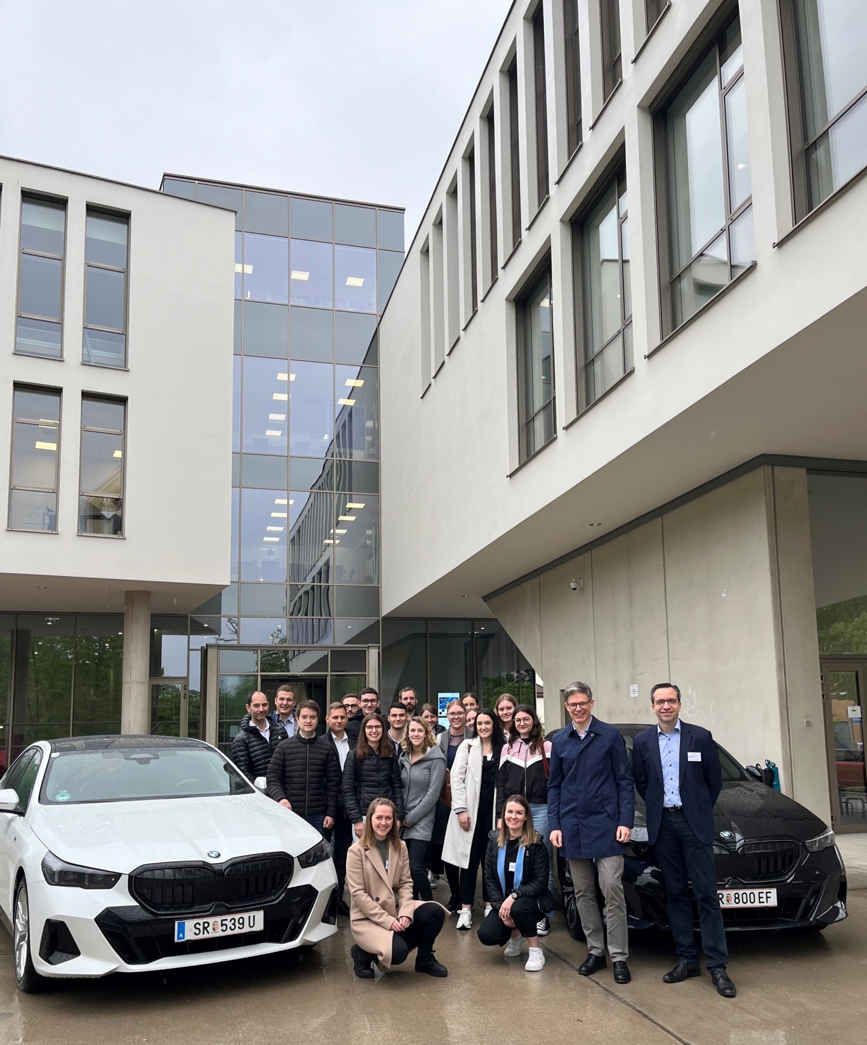 Gruppenfoto vor dem FH3-Gebäude: Menschen stehen in der Mitte, links und rechts von ihnen steht jeweils ein BMW-Auto