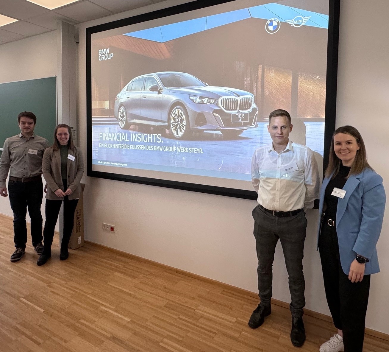 Zwei Vortragende stehen jeweils links und rechts der Präsentation des Vortrags von Financial Insights und lachen in die Kamera