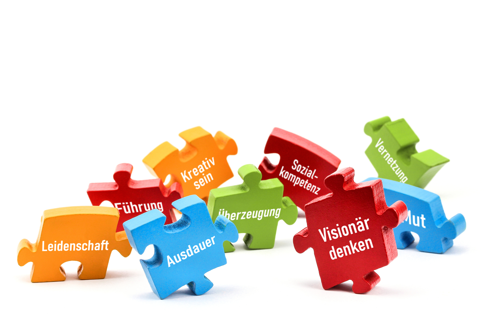 Verschiedenfarbige Puzzleteile, auf denen unterschiedliche Sozialkompetenzen stehen, zum Beispiel Ausdauer, Visionärsdenken und Kreativ sein