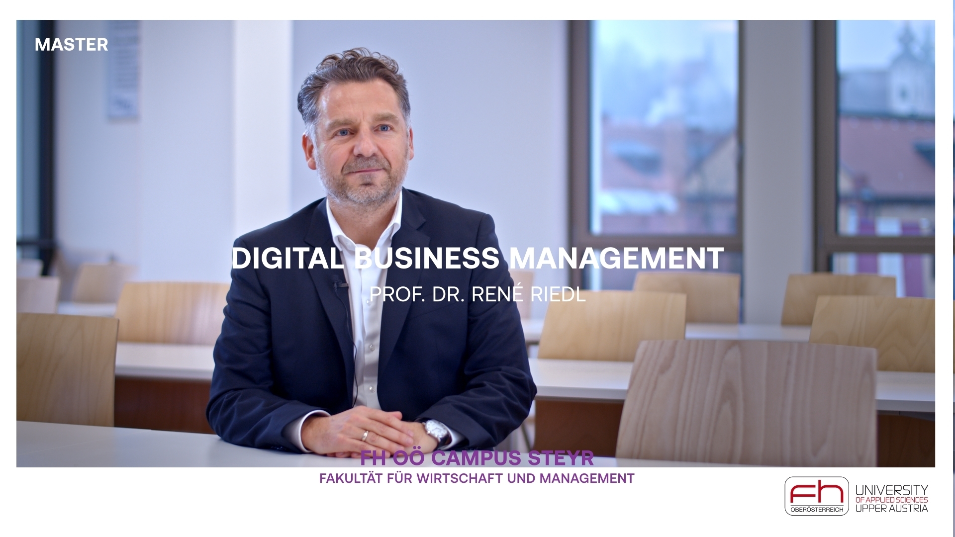 Prof. Dr. René Riedl sitzt an einem Tisch in einem Seminarraum und blickt in die Kamera. Vor ihm ist der weiße Text "Digital Business Management" eingeblendet. Unten in der Mitte steht "FH OÖ Campus Steyr – Fakultät für Wirtschaft und Management", rechts daneben befindet sich das Logo der FH OÖ