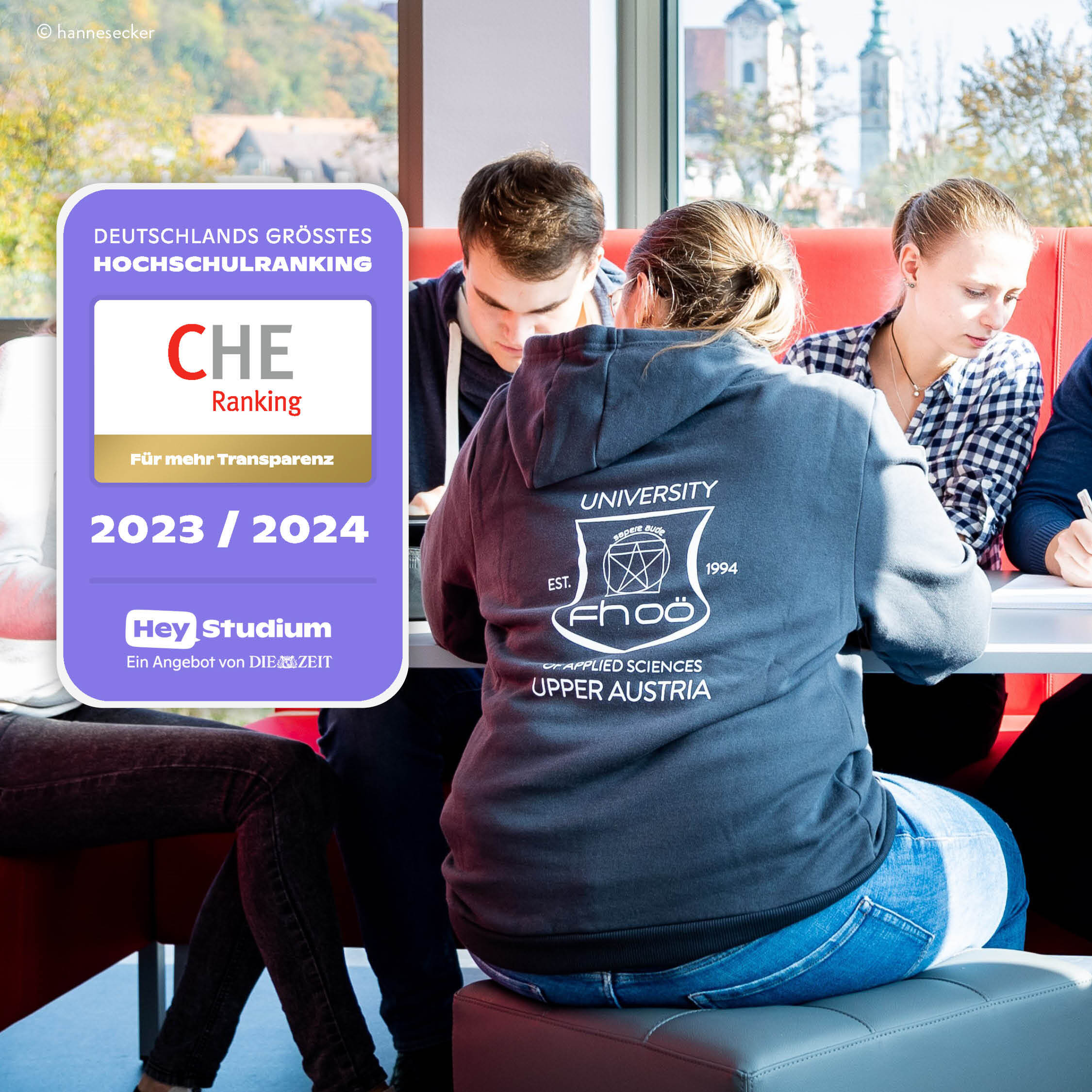 Mehrere Studierende sitzen an einem Tisch. Im Vordergrund ist der Rücken einer Person zu sehen, die einen Kapuzenpullover der FH OÖ trägt. Auf der linken Seite des Bildes befindet sich ein grafisches Overlay des Siegels des CHE-Rankings