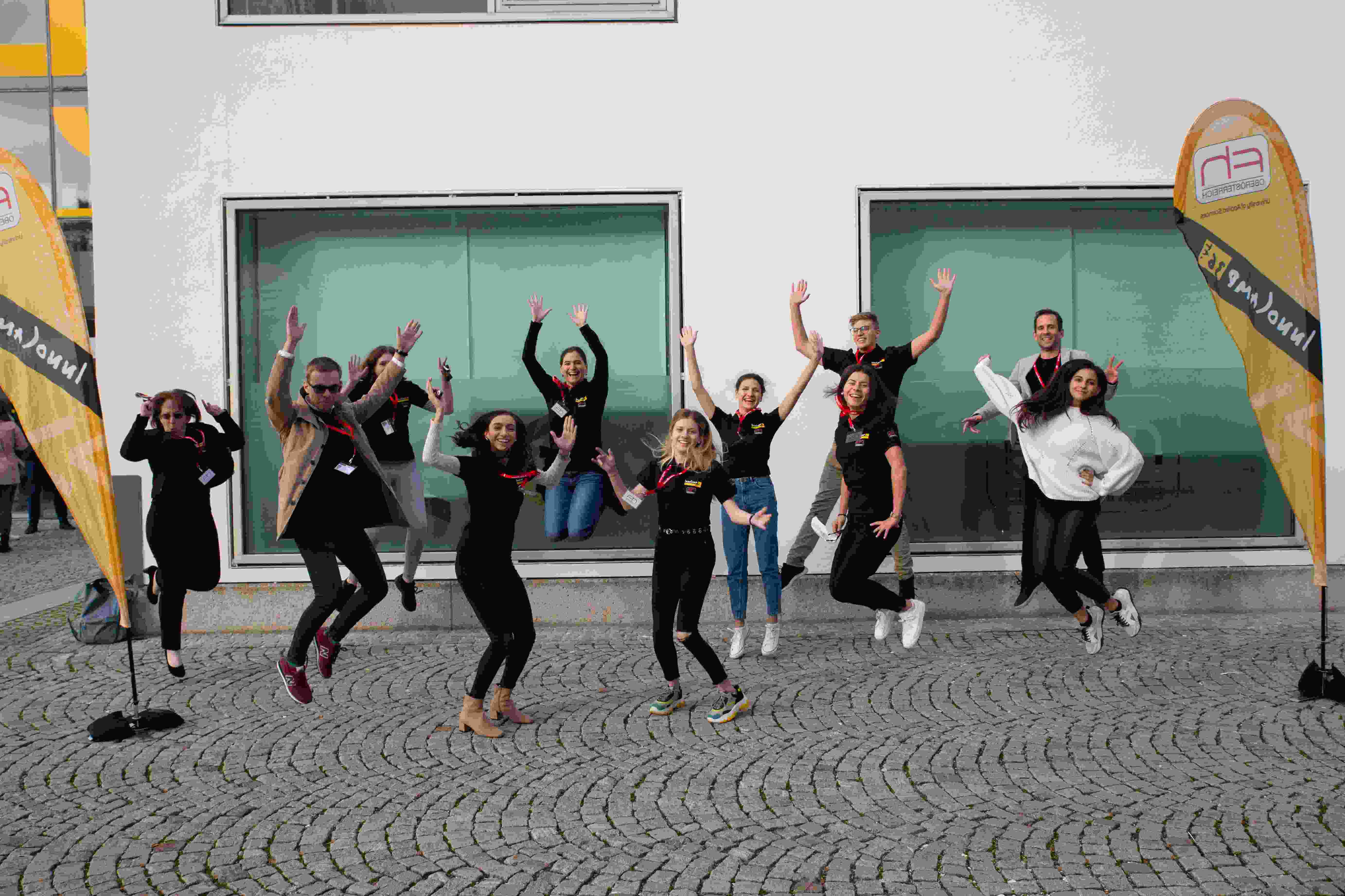 A group from Innocamp poses outdoors in front of a building with outstretched hands.