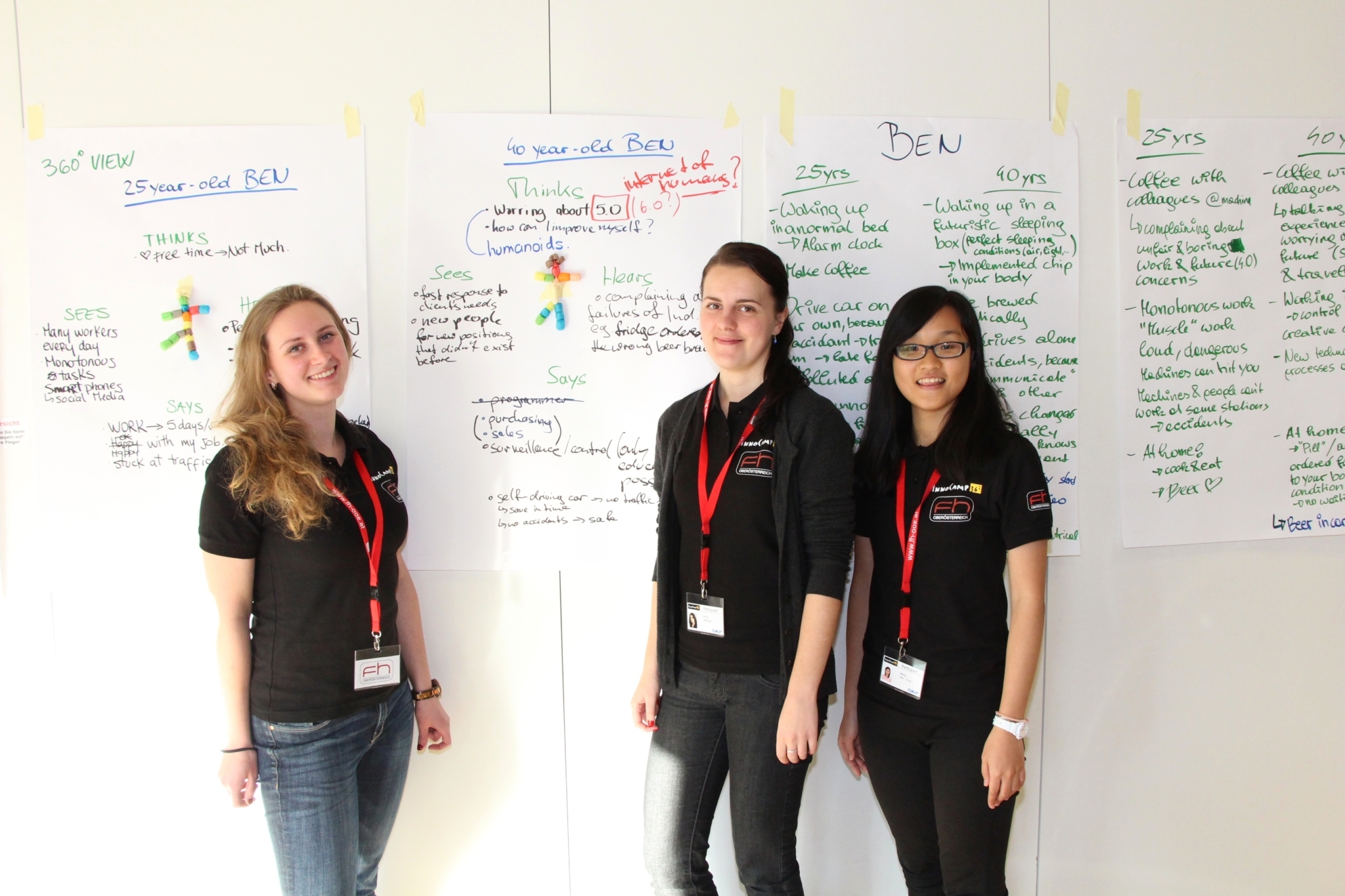 Three female students stand in front of posters that have been attached to a wall.