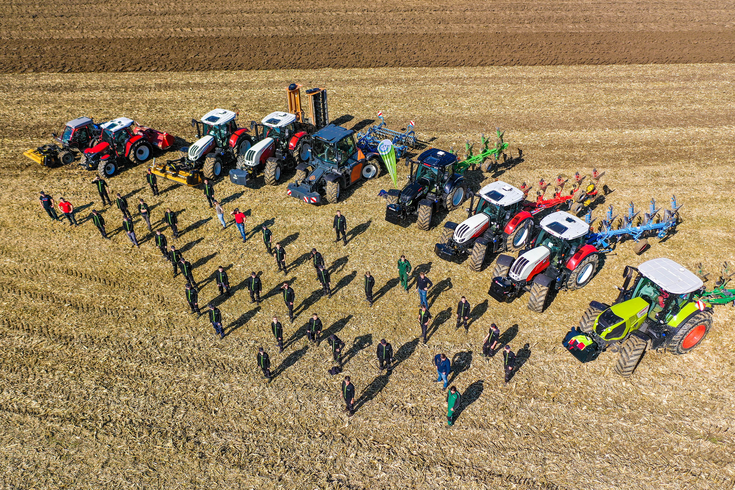 Eine Gruppe Studenten stehen vor verschiedenen Traktoren auf einem Feld und werden aus der Vogelperspektive gezeigt