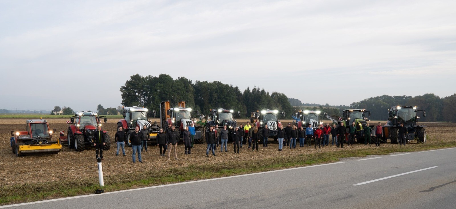 eine Gruppe Studenten stehen vor vielen Traktoren und werden von vorne gezeigt