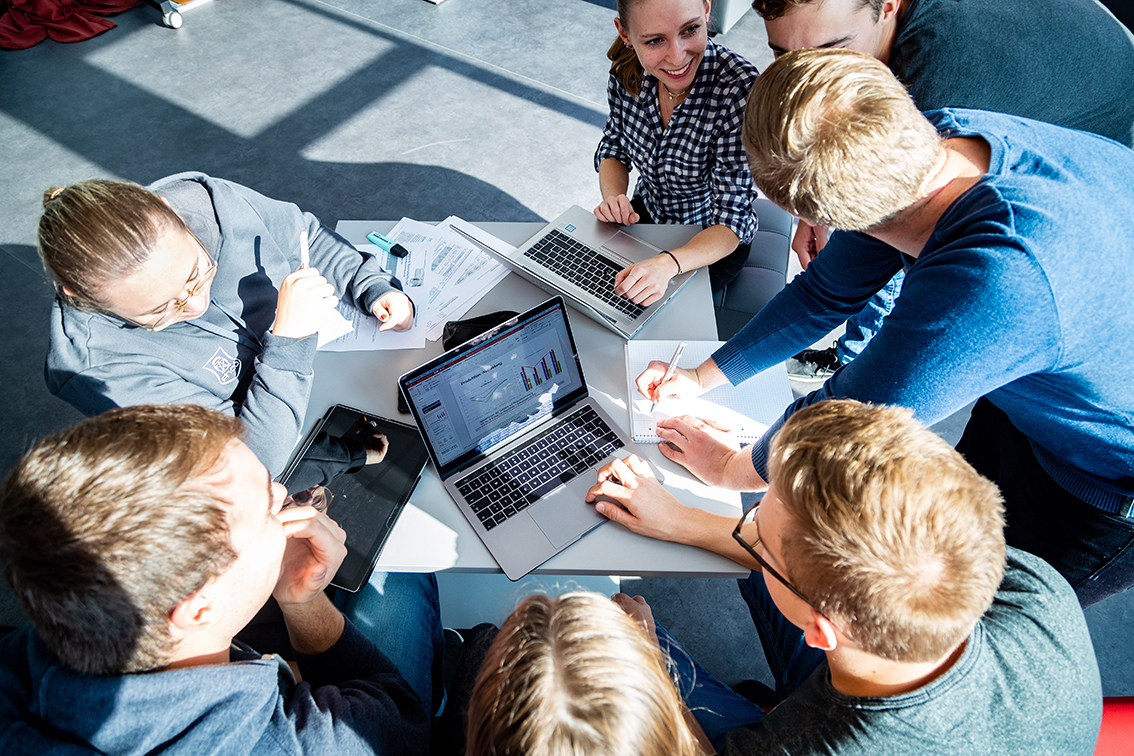 Eine Gruppe Studenten arbeitet mit ihren Laptops an einem Tisch