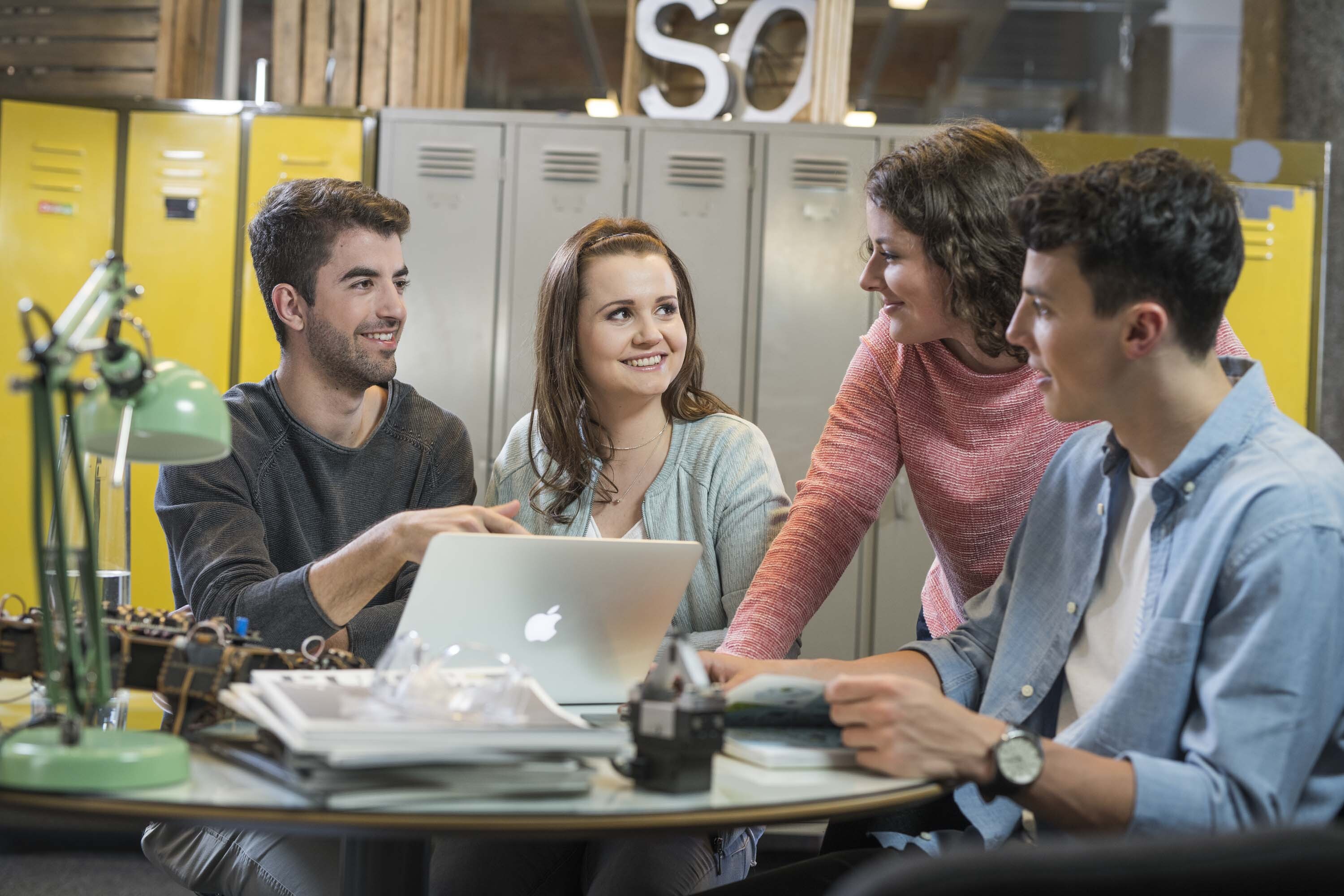 vier Studenten sitzen an einem Tisch und arbeiten an einem Laptop.