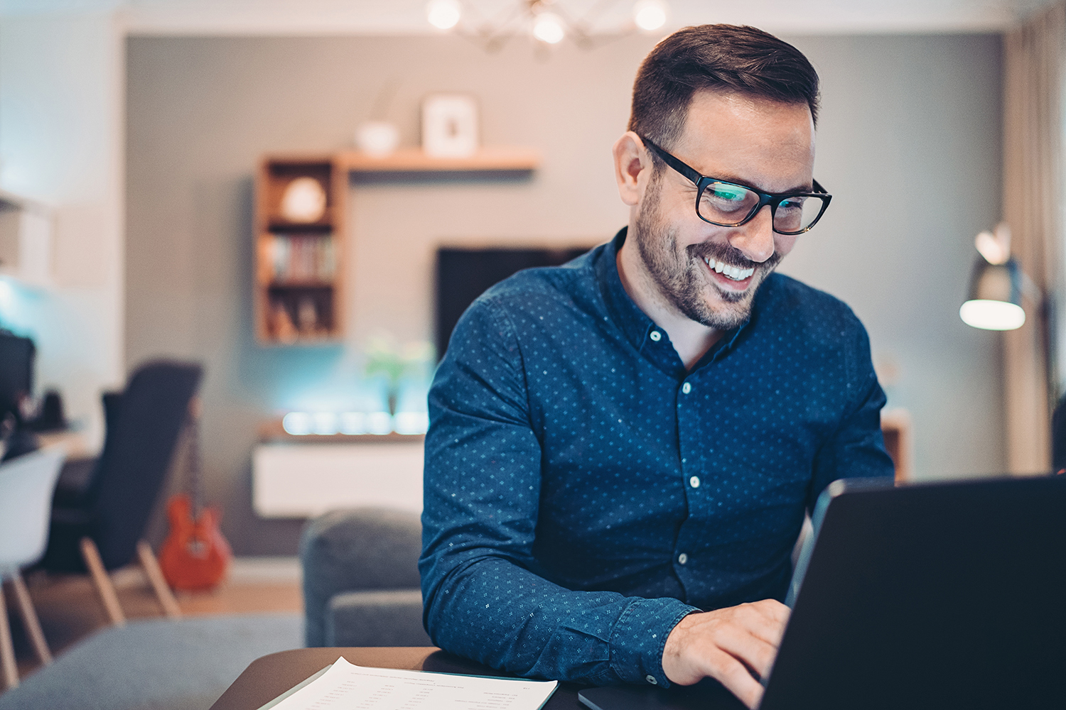 ein junger Mann sitzt mit einem Lächeln hinter seinem Laptop und arbeitet