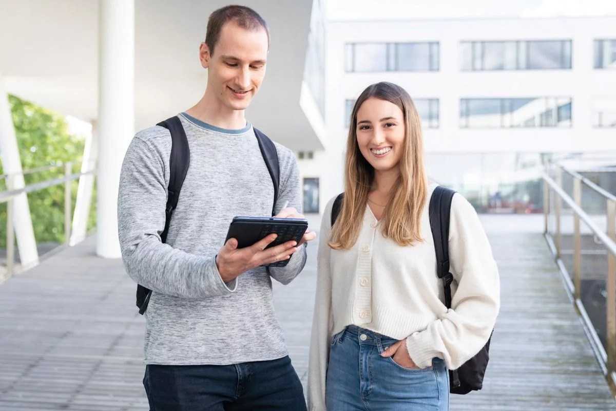 Ein Studierender und eine Studentin stehen am Campus Hagenberg. Der Mann hält ein Tablet in der Hand.