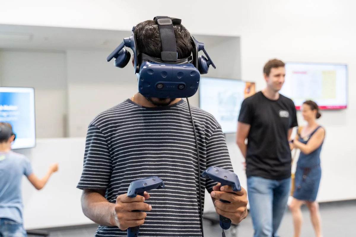 Ein junger Mann hat eine Virtual Reality Brille an und zwei Controller in der Hand