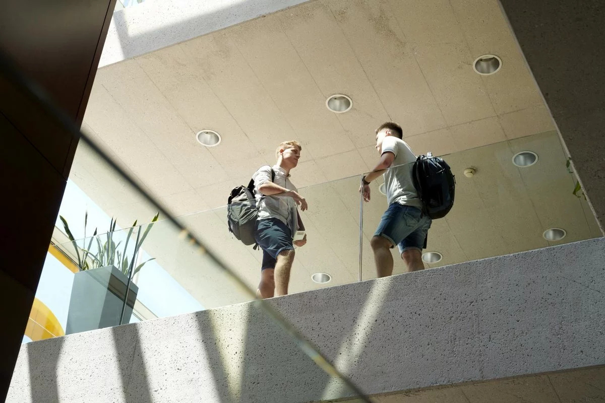 Zwei junge Männer stehen im 2. Stock in einem Gebäude an einem gläsernen Geländer