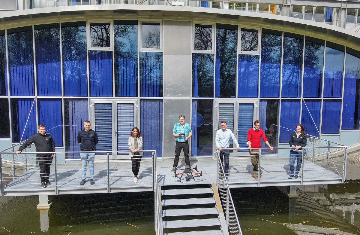 Zwei Frauen und fünf Männer stehen auf einem Balkon vor dem Campus Hagenberg. Vor dem Mann in der Mitt ist eine große Drohne