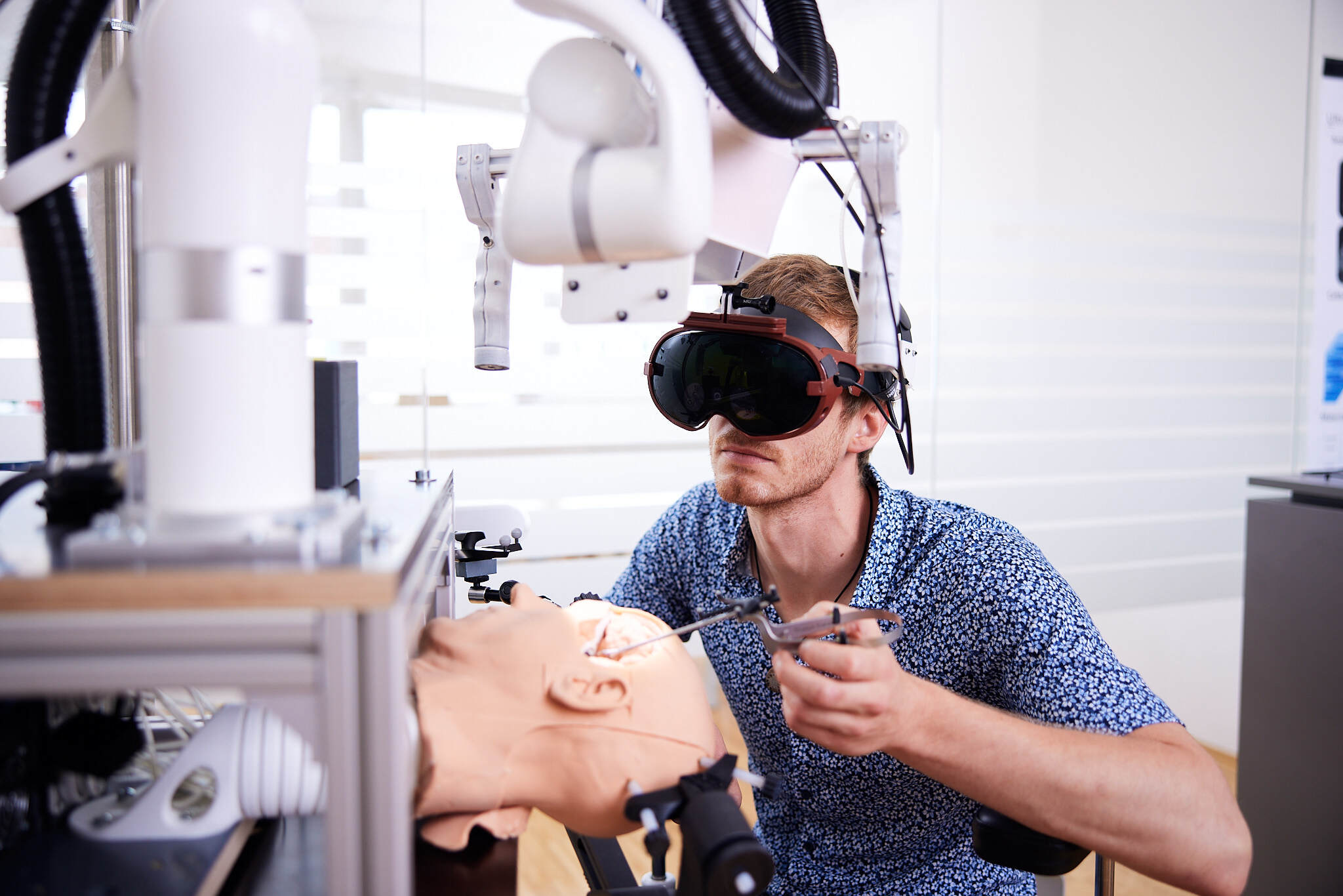 ein junger Student mit einem VR Headset operiert mit technischen Geräten an einem Test-Gehirn.