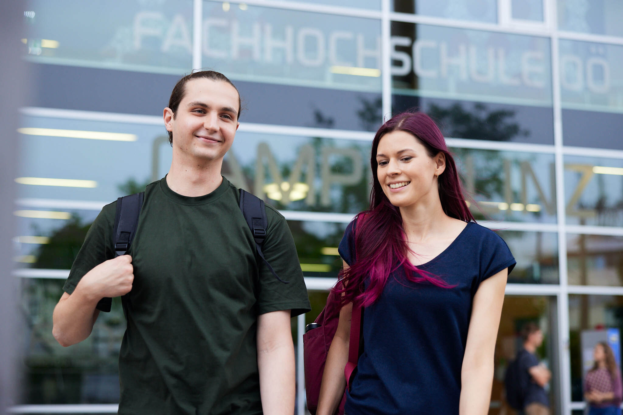 Zwei junge Studenten stehen vor einem Campusgebäude der FH Linz