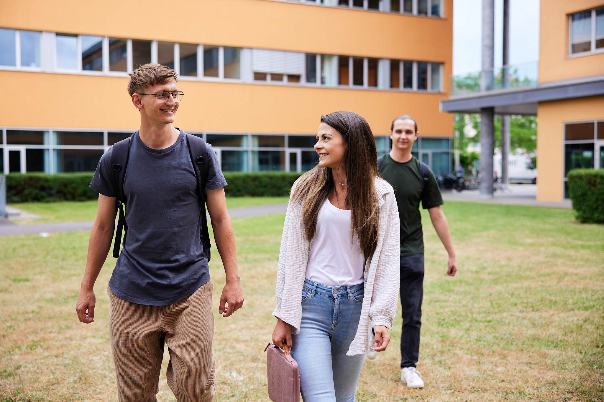 drei junge Studenten spazieren über eine Wiese am Campus Linz