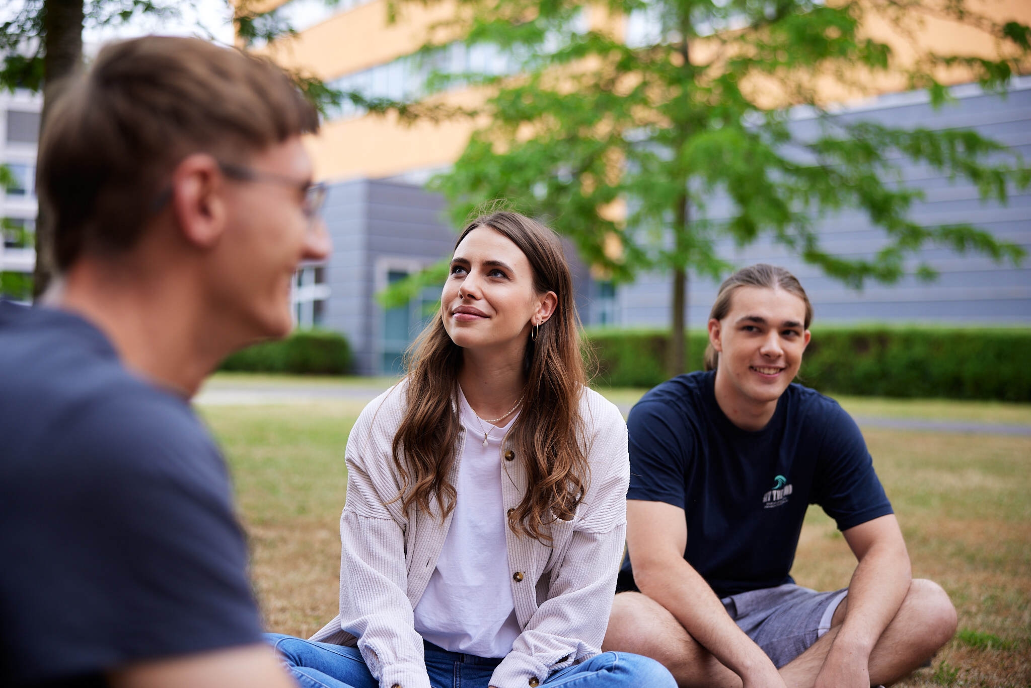 drei junge Studenten sitzen auf einer Wiese am Campus Linz